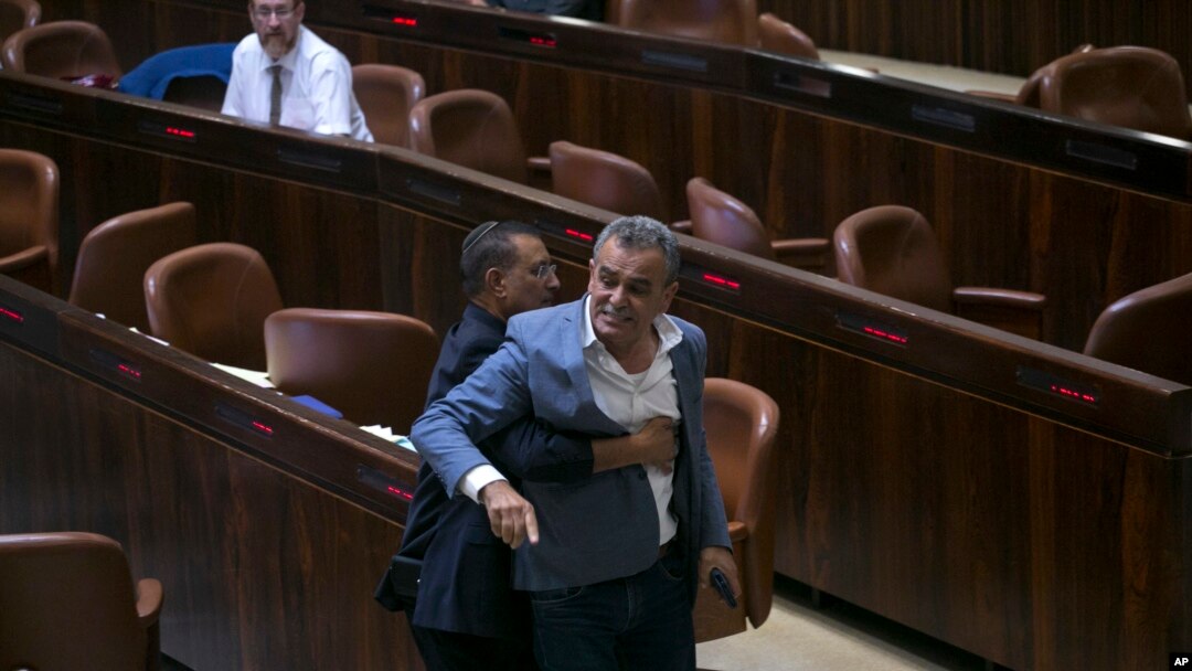 A Knesset usher removes Jamal Zahalka, an Israeli Arab member of the Knesset representing the Balad party, who was protesting the passage of a contentious bill, during a Knesset session in Jerusalem, Thursday, July 19, 2018. Israel's parliament approved a controversial piece of legislation early Thursday that defines the country as the nation-state of the Jewish people. Opponents and rights groups have criticized the legislation, warning that it will sideline minorities such as the country's Arabs.