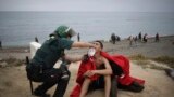 FILE — A man from Morocco is assisted by a Guardia Civil officer as he arrives swimming at the Spanish enclave of Ceuta, on May 18, 2021. 