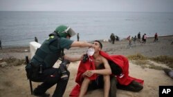 FILE — A man from Morocco is assisted by a Guardia Civil officer as he arrives swimming at the Spanish enclave of Ceuta, on May 18, 2021. 