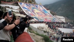 Tibetan Buddhists, tourists view a huge Thangka, a religious silk embroidery or painting displaying a Buddha portrait, during the Shoton Festival at Zhaibung Monastery in Lhasa, capital of southwest China's Tibet Autonomous Region, Aug. 25, 2014.