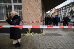 A woman stands beside candles and flowers placed as a tribute to victims of a shooting rampage in Hanau, Germany, Feb. 20, 2020.
