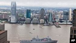 Crew members aboard the amphibious transport dock ship USS New York man the rails and present honors while passing The World Trade Center and the National September 11 Memorial and Museum as the ship arrives in Manhattan.