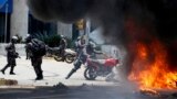 A Venezuelan Bolivarian National police officer drops a privately owned motorcycle into the flames after an explosion at Altamira square during clashes against anti-government demonstrators in Caracas, Venezuela, Sunday, July 30, 2017. 