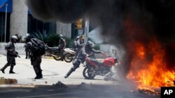 A Venezuelan Bolivarian National police officer drops a privately owned motorcycle into the flames after an explosion at Altamira square during clashes against anti-government demonstrators in Caracas, Venezuela, Sunday, July 30, 2017. 