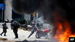 Seorang petugas Kepolisian Venezuela-Bolivia Venezuelan Bolivarian melempar sebuah sepeda motor milik pribadi ke kobaran api setelah terjadi ledakan di lapangan Altamira saat bentrokan dengan demonstran anti pemerintah di Caracas, Venezuela, Minggu, 30 Juli 2017. 