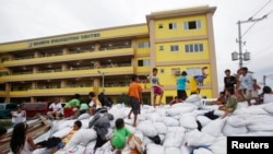 Timoun kap jwe sou yon pil sak manje sinistre nan yon sant nan vil Maniy kote yo pran refij apre pasaj Tifon Hagupit sou kòt peyi Filipin. Foto: 8 desanm 2014. 