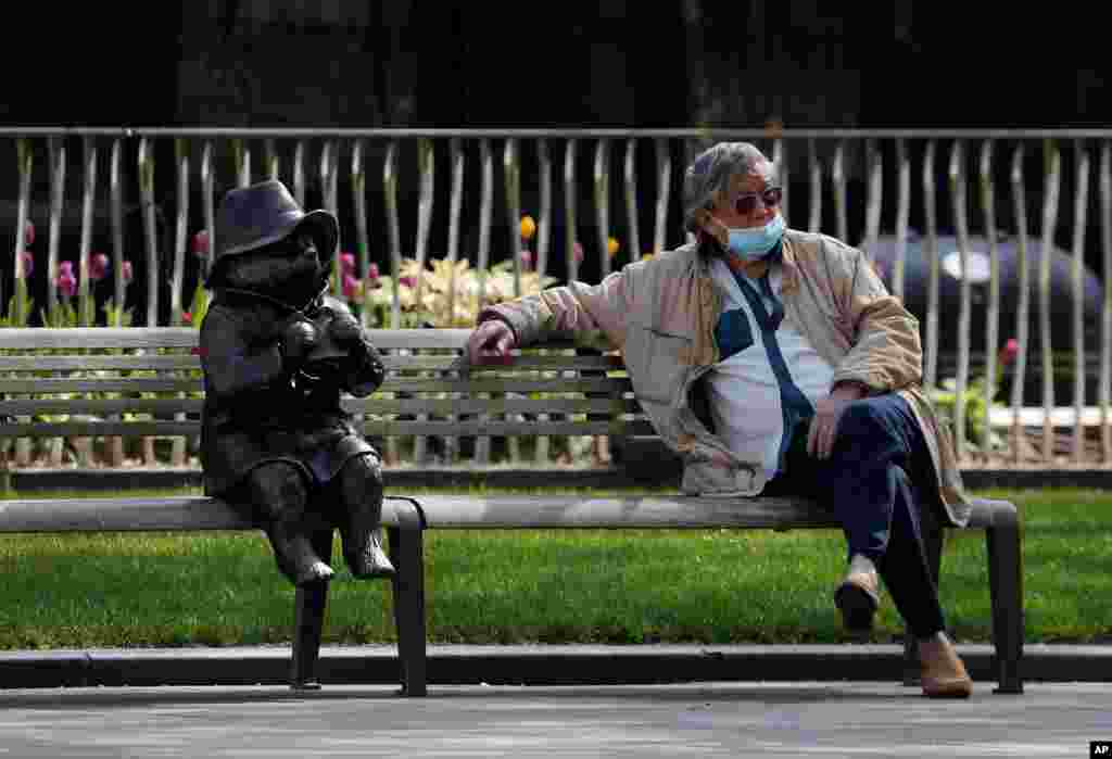 A man relaxes on a bench in London, next to a sculpture of Paddington Bear, as the country is in lockdown to help curb the spread of the coronavirus.