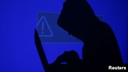 FILE - A hooded man holds a laptop computer in this illustration picture taken May 13, 2017. On Thursday, the United Arab Emirates denied targeted U.S. citizens in a hacking scheme.