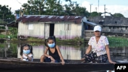 Una mujer y dos niñas usando mascarillas para protegerse del coronavirus se desplazan en un bote por el río Amazonas en Leticia, Colombia, el 13 de mayo de 2020.