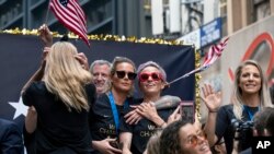 Members of the U.S. women's soccer team, including Megan Rapinoe, center and Julie Ertz, at right waving, celebrates during a ticker tape parade along the Canyon of Heroes, July 10, 2019, in New York.