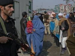 FILE - A policeman looks on as people wait to cross the Pakistan-Afghanistan border in the northwest town of Torkham, Nov. 27, 2011.