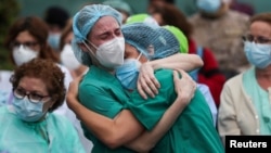 FILE - Health workers wearing protective face masks react during a tribute for their co-worker Esteban, a male nurse who died of complications related to COVID-19, outside the Severo Ochoa Hospital in Leganes, Spain, April 13, 2020.