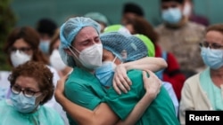 FILE - Health workers wearing protective face masks react during a tribute for their co-worker Esteban, a male nurse who died of complications related to COVID-19, outside the Severo Ochoa Hospital in Leganes, Spain, April 13, 2020.