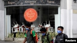 Personas con mascarilla pasan frente a un restaurante cerrado durante la cuarentena por el coronavirus en Caracas, Venezuela. Marzo 20 de 2020.