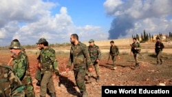 Forces loyal to Syria's President Bashar al-Assad walk in al-Mallah Farms, as fires burn alleged warehouses for the rebels in the background. Government troops said they regained control of the area north of Aleppo, Dec. 15, 2014. 