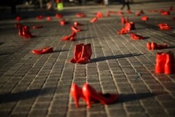 Passers-by walk past dozens of red painted shoes placed on the ground as a part of an installation against violence against women in Brussels, Nov. 25, 2019.