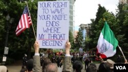 Protesters hold signs as they face off in Portland. (R. Taylor/VOA)