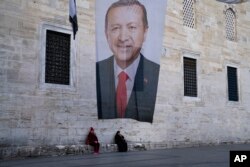 FILE—Two women sit near a campaign banner of Turkish President and leader of the Justice and Development Party, or AKP, Recep Tayyip in Istanbul, Turkey, March 11, 2024.