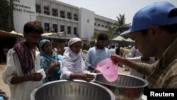 Warga menerima air minum dari sukarelawan di meja yang digelar di luar Jinnah Postgraduate Medical Center (JPMC) di tengah panas terik di Karachi, Pakistan (23/6). (Reuters/Akhtar Soomro)