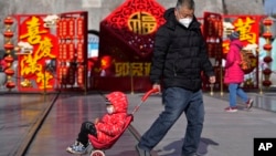 资料照：一名男子拉着一个孩子的推车走在北京前门的购物街上。（2023年1月17日）