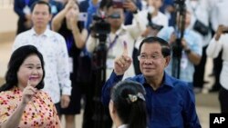 Perdana Menteri Kamboja Hun Sen (kanan) dan istrinya Bun Rany (kiri) memperlihatkan jari telunjuk yang sudah ditandai tinta usai memasukkan surat suara di sebuah TPS di Takhmua, Provinsi Kandal, Pnom Penh, Kamboja, Minggu 23 Juli 2023. (Foto: Heng Sinith/AP Photo)