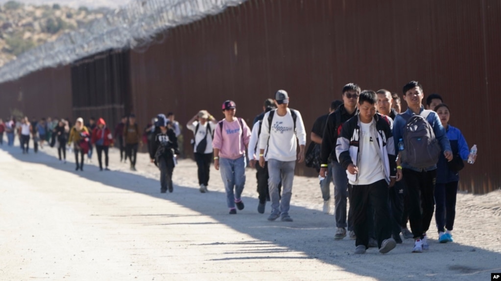 FILE - Migrants from China and elsewhere walk along a wall after crossing the U.S. border with Mexico to seek asylum, near Jacumba, California, Oct. 24, 2023.