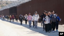 FILE - Migrants from China and elsewhere walk along a wall after crossing the U.S. border with Mexico to seek asylum, near Jacumba, California, Oct. 24, 2023.