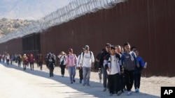 FILE - A group of people, including many from China, walk along the wall after crossing the border with Mexico to seek asylum, near Jacumba, California, Oct. 24, 2023. 