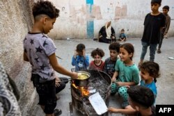 Anak-anak duduk bersama di sekitar seorang anak laki-laki yang memasak mie instan di atas api dalam oven darurat dari tong daur ulang, di Rafah di Jalur Gaza selatan pada 31 Oktober 2023. (Foto: AFP)