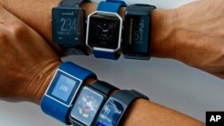 FILE - Six fitness tracking devices measuring step counts and other fitness features are worn, July 20, 2016. Clockwise, from top left are the Garmin Vivoactive, Fitbit Blaze, Garmin Vivoactive HR, Samsung Gear Fit2, Apple Watch and Fitbit Surge. 