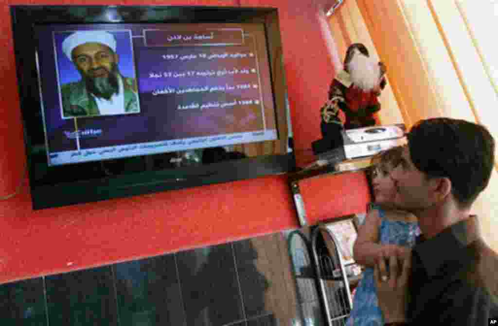 A man holds his daughter while watching a TV broadcast on the death of Osama bin Laden in Basra, Iraq, Monday, May 2, 2011 (AP Photo/Nabil al-Jurani)