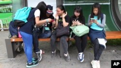 FILE - South Korean middle school students use their smartphones at a bus station in Seoul, South Korea.