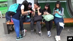 FILE - South Korean middle school students use their smartphones at a bus station in Seoul, South Korea, May 15, 2015.