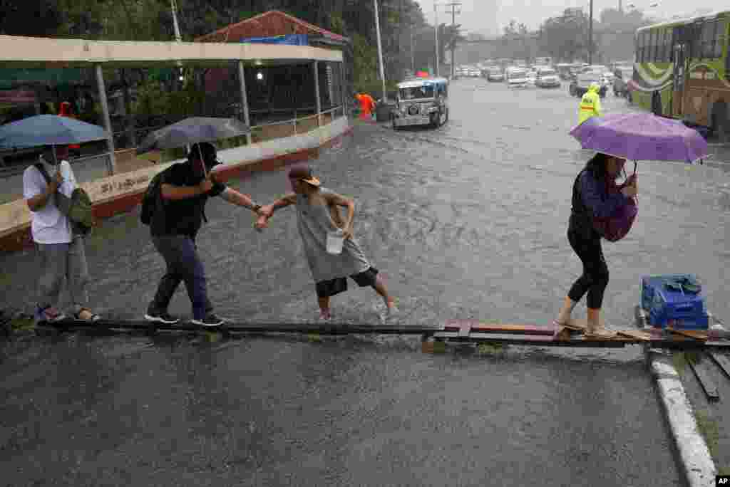 Commuters cross a flooded street on a wooden plank after heavy rains from tropical storm "Nesat" inundated some parts of metropolitan Manila, Philippines.