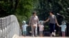 In this June 1, 2017 photo, women walk with children wearing matching hats as they cross a bridge at a public park on International Children's Day in Beijing. 