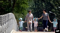 In this June 1, 2017 photo, women walk with children wearing matching hats as they cross a bridge at a public park on International Children's Day in Beijing. 