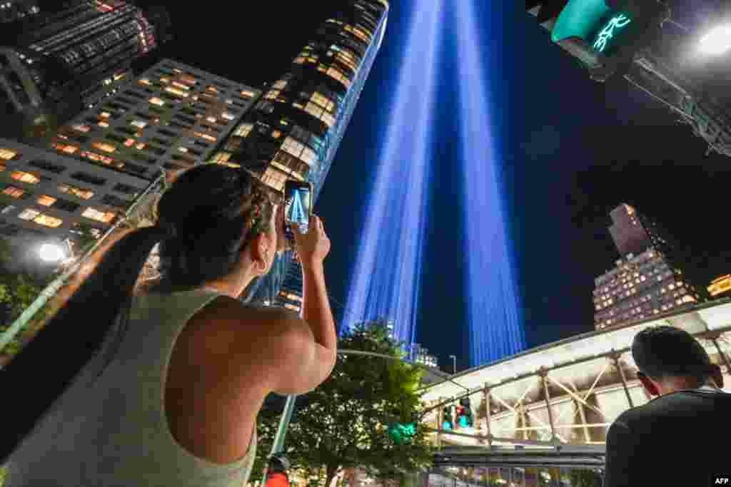 TOPSHOT - A person takes a photo of the 'Tribute in Light' public art installation commemorating the 9/11 2001 terrorist attacks as it shines up from the skyline of lower Manhattan in preparation for the 25th anniversary, in New York City, on September 10, 2026. (Photo by Ryan MURPHY / AFP)