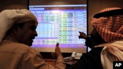 Saudi traders chat as they follow a screen displaying Saudi stock market values at the Arab National Bank in Riyadh, Saudi Arabia.