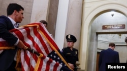 Staff members carry American flags back into the office of the Speaker of the House after they were used as a backdrop while former Speaker of the House Kevin McCarthy spoke after being ousted from the position of speaker on Oct. 3, 2023. 