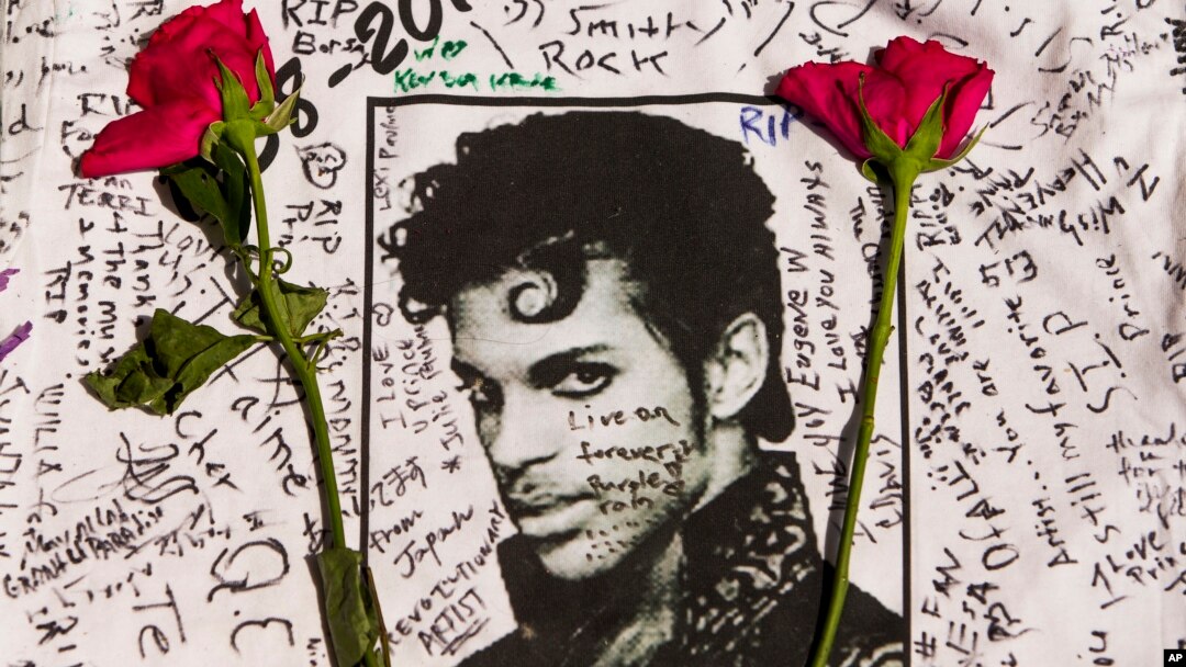 FILE - Flowers lie on a T-shirt signed by fans of singer Prince at a makeshift memorial created outside Apollo Theater in New York, April 22, 2016.