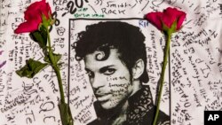 FILE - Flowers lie on a T-shirt signed by fans of singer Prince at a makeshift memorial created outside Apollo Theater in New York, April 22, 2016.