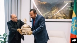 Ethiopia's Prime Minister, Abiy Ahmed, right, with gloved hands as he officially hands over a crown to the country's tourism minister, Hirut Kassaw, Feb. 20, 2020.