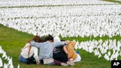 Visitors sit among white flags that are part of artist Suzanne Brennan Firstenberg's temporary art installation to commemorate Americans who have died of COVID-19, on the National Mall in Washington, Sept. 21, 2021. 