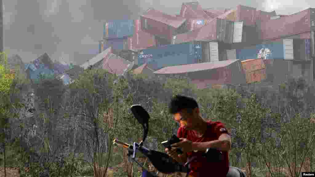 Un homme vérifie son téléphone portable à proximité des conteneurs maritimes endommagés par l'explosion, Tianjin, 13 août 2015.