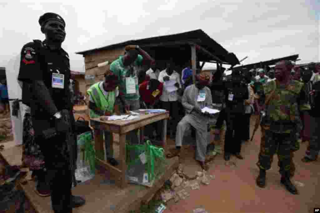 Soldiers of the Nigerian army, right, and a policeman, left, stand guard as electoral officials count ballot papers after the National Assembly election in Ibadan, Nigeria,Saturday, April 9, 2011.