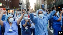 Nurses and medical workers react as police officers and pedestrians cheer them outside Lenox Hill Hospital, April 15, 2020, in New York. 