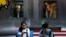 Shoppers sit on a bench with a decorated U.S. flag browsing their smartphones outside a fashion boutique selling U.S. brand clothing at the capital city's popular shopping mall in Beijing, Sept. 24, 2018. 