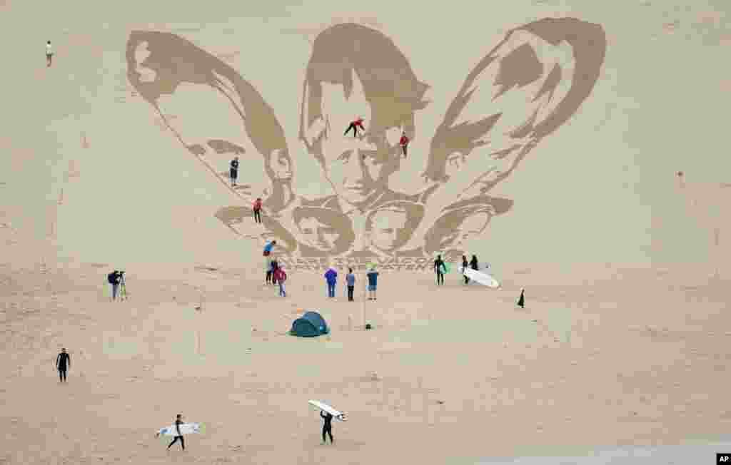 Surfers and sunbathers look on as activists place the finishing touches on a drawing in the sand of the heads of G-7 leaders at the the beach in Newquay, Cornwall, England.