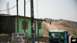 A woman walks near a sign that reads 'I made holes for burials' in Spanish, near a cemetery in Ventanilla, on the outskirts of Lima, Peru, Aug. 12, 2020.