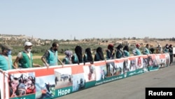 Healthcare workers hold signs near Bab al-Hawa crossing during a sit-in against its closure, at the Syrian-Turkish border, in Idlib governorate, Syria, July 2, 2021.